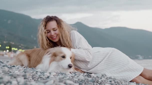 Best friends tender moment. Young curly girl lying on rocks with her border collie dog. Pretty woman relaxing at the beach with her dog at sunset on the background of mountain. Concept of friendship — Stock Footage Best friends tender moment. Young curly girl lying on rocks with her border collie dog. Pretty woman relaxing at the beach with her dog at sunset on the background of mountain. Concept of friendship Royalty Free Stock Footage