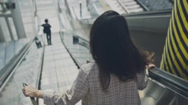 Havaalanında yürüyen merdivenden inen genç bir iş kadını. Güzel bir kadın bagajıyla hareket ediyor, terminale bakıyor. İş gezisi için uçağa binen bir kız. Seyahat ve iş kavramı.