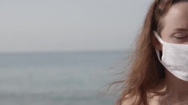 Halk plajında koruyucu maske takan genç bir kadının yarım portresi. Koronavirüse karşı önlem kavramı. Salgın sırasında sağlık ve güvenlik hayatı, N1H1