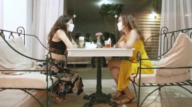 Sosyal uzaklık. Kafede ya da restoranda maske takan iki kadın. Salgın covid-19 'dan sonra yeni kurallar. Virüse karşı önlem.