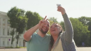 Yaşam tarzı, arkadaşlık ve şehir tatili kavramı. Şehrin arka planında selfie çeken farklı arkadaşlarınız kutlu olsun. İki gülümseyen şişman vücut pozitifliği olan insan kendi portresini yapıyor. Yaz tatilleri.