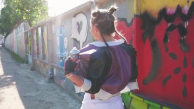 Neşeli kız yürüyor ve havaya sprey boya sıkıyor. Özgürlük ve yaşam tarzı kavramı. Yaratıcı genç grafiti sanatçısı sıcak yaz gününde boyalı duvara karşı eğleniyor. Vahşi ve özgür.