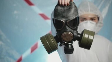 Koruyucu giysili ve solunum cihazlı kadın bir virüs uzmanı gaz maskesi tutuyor. Coronavirus 'a karşı sağlık savaşı. Salgın ve salgın COVID karantina konsepti. Hastane, klinik ve laboratuvar için model.