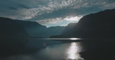Dağlardaki çarpıcı göl manzarası. Rüzgarlı havanın manzarası, akan su, bulutların arasından geçen güneş ışığı. Diğer tarafında orman olan güzel bir sahil şeridi. Doğa kavramı, seyahat.