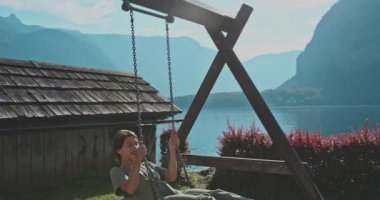 Salıncakta sallanan kaygısız genç bir kadın arka planda muhteşem bir doğa ile harika vakit geçiriyor. Kız anın tadını çıkarıyor ve ağaçlı ve suyla dağların görkemli manzarasına hayran. Seyahat kavramı, güzellik.