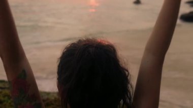 Güzel esmer, okyanus kıyısında meditasyon yapıyor. Kadın elleri altın gün batımının önünde yoga egzersizleri yapıyor. Genç kızın vücudu incedir. Sağlık hayatı kavramı. Meditasyon, rahatlama, özgürlük. mutluluk.