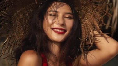 Sıcak yaz gününde hasır şapkalı ve kırmızı elbiseli güzel melez bir kadın. Güzel Asyalı kız gülümsüyor. Güzellik, seyahat, tatiller, moda konsepti ve yaşam tarzı.