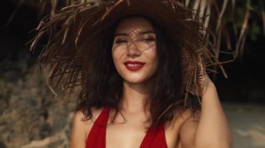 Hasır şapkalı, yaz tatilinde kırmızı elbiseli ve kameraya poz veren ve gülümseyen şehvetli genç bir ırk kadını. Güzellik, seyahat, tatiller, moda konsepti ve yaşam tarzı.