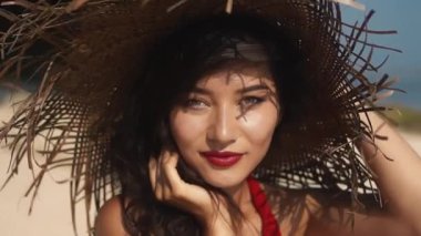 Sıcak yaz gününde hasır şapkalı ve kırmızı elbiseli genç melez bir kadın. Lüks, şehvetli Asyalı kız portresi kameraya gülümsüyor. Güzellik, seyahat, tatiller, moda yaşam tarzı.
