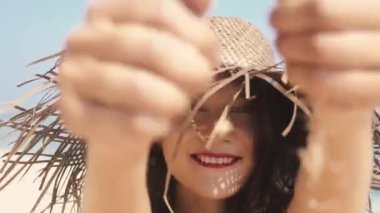 Kırmızı elbiseli güzel bayan cennet adasının tadını çıkarıyor, güneş parlıyor. Romantik ve sakin bir ruh hali. Bali 'nin seyahat yaşam tarzı. Hasır şapkalı neşeli Asyalı kadın parmaklarının arasındaki kumu temizliyor..