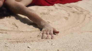 Güzellik, kaplıca, özgürlük konsepti. Beyaz kumda uzanan ve rahatlatan seksi kırmızı elbiseli Asyalı çekici kadın. Erotik ruh hali. Sahilde yoga yapan bir kız. Ellerinle kuma dokunuyorsun. Vücut uygulaması.