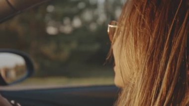 Yaşam tarzı ve güzellik kavramı. Gün batımında arabasını süren şık güneş gözlüğü takan sevimli sarışın yüzün yakın çekimi. Güzel kız seyahat ederken sakin müzikler dinliyor ve dinleniyor..