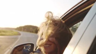 Arabada oturan ve yolcu vagonunun camından sarkan güzel sarışın kızın portresi. Kameraya gülümseyen şık bir kadın. Koyu renk saçları rüzgarda dalgalanıyor. Seyahat kavramı.