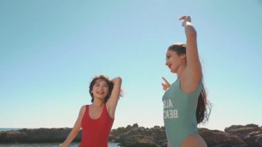 Muhteşem deniz sahillerinde poz veren iki güzel genç kız. Sıcak yaz melteminin tadını çıkaran kadınlar, mavi gökyüzünün altında kumlu sahilde zıplayan ve el sallayan kadınlar. Tatil, seyahat, gençlik kavramı.