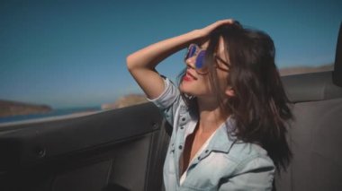 Cabriolet 'in yolcu koltuğunda oturan çekici genç kız muhteşem Akdeniz kıyısından geçiyor. Yaz rüzgarı dalgalı saçlarıyla gülen bir kız. Seyahat, tatil, macera kavramı.