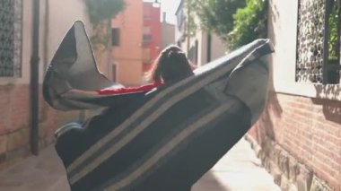 Çekici genç Asyalı kadın şık kırmızı bir kazak giymiş çizgili pançosunu sallıyor ve öpücük yolluyor. Küçük bir sokakta koşuşturan ve İtalya 'da maceralara hazır eğlenceli bir kız..