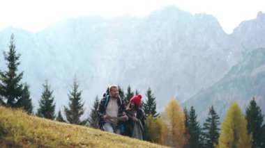 Büyük sırt çantalı adam ve tepenin kenarında duran ve kağıt harita okuyan ya da yol arayan bir kız. Kadın el hareketleriyle yolu gösteriyor. Genç turist ailesi doğa yürüyüşü ya da yürüyüş yapıyor..