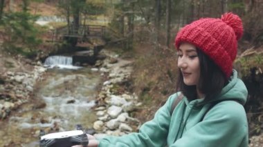 Dron ya da kuadrokopteri havaya fırlatan kızın yüzünün ve ellerinin yakın çekimi. Dağ nehrinin yakınında bir kadın İHA ya da helikopteri gökyüzüne gönderiyor. Kadın doğada yalnız zaman geçiriyor. Seyahat ya da turizm konsepti.