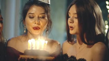 Partide ya da doğum günü şapkalı Asyalı bir kız evinde ya da evinde tatil partisinde dilek diliyor. Doğum günü pastasında mum üfleyen ve tebrik eden çok ırklı genç bayan arkadaşlarının portresi..