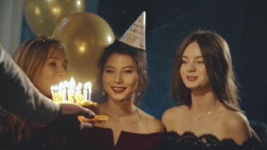 Genç bir kadın mumlara ateş üflüyor ve partilerde ya da kutlamalarda dilek tutuyor. Gülümseyen Asyalı kız ve arkadaşlarının yakın plan portresi. Sürpriz yapıyorlar ve mumlarla doğum günü pastasını çıkarıyorlar..