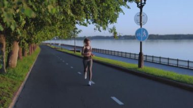 Güzel sporcu kadın maratona hazırlanıyor. Rıhtım boyunca sabah koşusu. Sokakta ya da güneş doğarken parkta egzersiz yapmak. Koşucu kardiyo yapıyor. Sağlık ve sağlıklı yaşam tarzı kavramı.