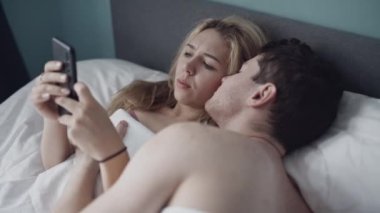 Genç evli çiftin cep telefonuyla ya da ellerinde akıllı telefonuyla yatakta yattığı orta boy bir fotoğraf. İnternet ya da sosyal ağlara bağımlı bir kadın. Modern teknolojiden kaynaklanan ilişki sorunları.