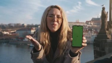 Yeşil ekranda akıllı telefonu tutan güzel bir kız. Krom anahtarı olan akıllı bir telefondan mobil bir uygulamanın reklamını yapan çekici bir genç kadın. Teknoloji ve cihaz kavramı