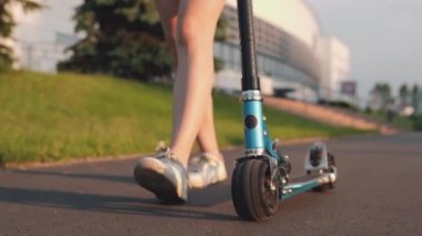 Mavi scooter 'la kaldırımda yürüyen genç bir kadının ayağı ya da bacağı. Gün batımında parkta yürüyen bir kız. Ergen gün ışığında yalnız zaman geçirir. Üniversite hayatı kavramı, buz pateni, yaz zamanı..