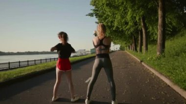 Genç seksi çok ırklı kadınlar nehir kenarında koşmadan önce kaslarını esnetiyorlar. Güzel kızlar kollarını ve bacaklarını ovalarlar. Eğitimden önce ısın. Sağlıklı yaşam tarzı kavramı