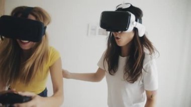 Evde sanal gerçeklik kasklı güzel kızlar var. Modern sanal gerçeklik kulaklıklarıyla video oyunları oynayan ve birlikte eğlenen iki kadın. Üç boyutlu teknoloji. Sanal gerçeklik, oyun, arkadaşlık kavramı.