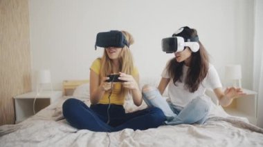 Evde sanal gerçeklik kasklı güzel kızlar var. Modern sanal gerçeklik kulaklıklarıyla video oyunları oynayan ve birlikte eğlenen iki kadın. Üç boyutlu teknoloji. Sanal gerçeklik, oyun, arkadaşlık kavramı.