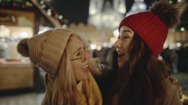 Çekici lezbiyen kızlar yılbaşı arifesinde festival sokak fuarında tanışan ve kucaklaşan çiftler. LGBT toplum temsilcileri hoş vakit geçiriyorlar, bayram atmosferini ve yanan maytapları birleştiriyorlar