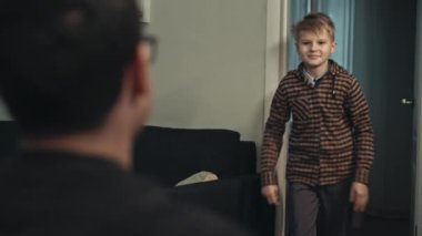 Genç baba sonunda işten eve geliyor. Babasına koşan ve ona sarılan sıradan giysili mutlu ergen oğlanın yakın çekimi. Gülümseyen oğul, akşam babasını kapıda karşılıyor. Mutluluk kavramı.