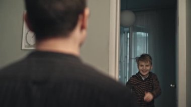 Gülümseyen oğul, akşam babasını kapıda karşılıyor. Mutluluk kavramı. Babasına koşan ve ona sarılan sıradan giysili mutlu ergen oğlanın yakın çekimi. Genç baba sonunda işten eve geliyor..