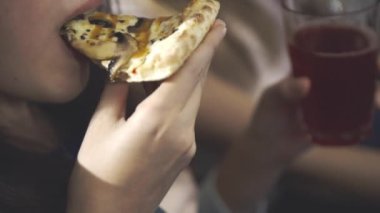 Arkadaşlar konuşur, güler, yemek dağıtırlar. Mutlu yüz ve elinde bir dilim pizza ve bardakla içki tutan bir kızın yakın çekimi. Oturma odasında pizza ve televizyonlu ev partisi..