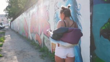 Özgürlük ve yaşam tarzı kavramı. Neşeli kız yürüyor ve havaya sprey boya sıkıyor. Yaratıcı genç grafiti sanatçısı sıcak yaz gününde boyalı duvara karşı eğleniyor. Vahşi ve özgür.