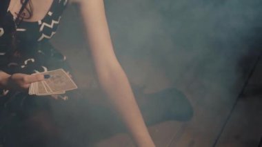 Ezoterik ayin sırasında tarot kartları yerleştiren bir kadın. Falcı kartları koyarak kaderini tahmin ediyor. Arka planda yanan mum, duman ve kafatası olan ürkütücü mistik bir atmosfer. Kehanet kavramı.