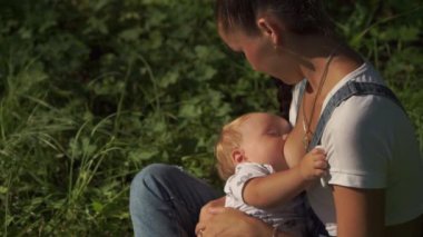 Parkta emziren bir çocuğun portresi. Yeşil ağaçlarla çevrili bir bebeğin anne göğsünü içtiği duygusal sahne. Toplu beslenmenin modern ilerici yaşam tarzı. Annelik kavramı.
