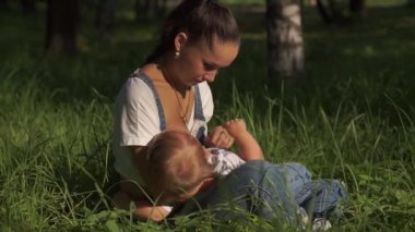 Parkta bebeği besleyen, yerde oturan genç bir annenin portresi. Yeşil doğayla çevrili bir kadın, emzirirken çocuğuyla oynaşıyor. Toplum içinde beslenen ilerici annelik.