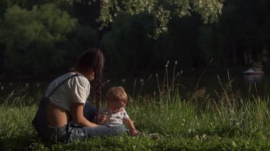 Bekar anne kavramı. Anne ve bebeğinin parkta güzel bir sahnesi. Anne bebeğe çiçek veriyor ve çocuk el sallıyor. Çevredeki dünyayı öğrenen, doğayı deneyimleyen çocukların duygusal portresi..
