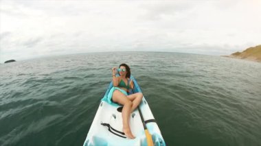 Genç ve güzel bir kadın güneşli bir havada mavi tropikal denizde kano üzerinde kürek çekiyor. Bora Bora 'da mayo giymiş, güneş gözlüklü mutlu bir kız. Aktif yaşam tarzı ve spor anlayışı. Tatiller ve tatiller.