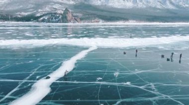 Donmuş göl yüzeyinde paten kayan bir grup yolcuyu takip eden insansız hava aracı çekimi. Doğanın güzelliklerini keşfeden turistler dağ sırasının görkemli arka planına ve güzel buzlu pürüzsüz buzlara sahipler.