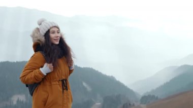 Mutlu Asyalı kadın turist soğuk havada bulutlu dağlarda temiz hava solumaktan hoşlanır. Dağ manzarasının dumanlı arka planında genç bir yürüyüşçü. Etkin yaşam biçimi kavramı