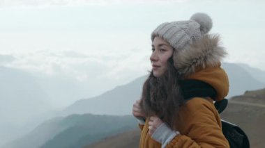 Soğuk havada bulutlu dağlara bakan çok ırklı kadın turistin portresi. Dağ manzarasının dumanlı arka planında genç bir yürüyüşçü. Etkin yaşam biçimi kavramı