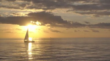 Okyanus dalgalarında yüzen yalnız yatın silueti. Yalnız yelkenli açık denizde altın gün batımında sürüklenir. Su taşımacılığı kavramı, denizcilik gemisi.