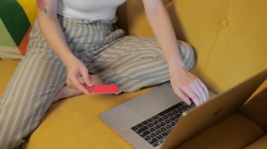 İnternetten alışveriş yapan mutlu bayan alışverişçi kolay taşınabilir ödemeler yapıyor. Evde dizüstü bilgisayarla oturmuş, elinde kredi kartı olan gülümseyen genç bayan müşteri. E-bankacılık uygulama servisi