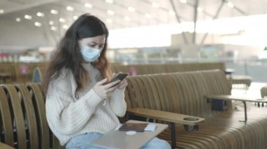 Tıbbi maske takan genç bir kadın havaalanı terminalinde telefonla uçuş kaydı yaptırmaya çalışıyor. Yolcunun kayıt uygulaması ile ilgili sorunu var. Web sitesinde hata. Coronavirus salgınında seyahat