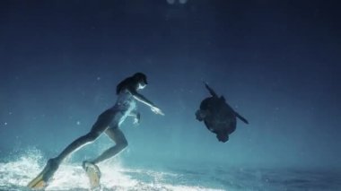 Açık mavi denizde kızla yüzen yeşil tropikal kaplumbağa. Doğal ortamında su altında yüzen güzel bir serbest yüzücü ve kaplumbağa. Sualtı sahnesi doğadaki tropikal kaplumbağaları izliyor..