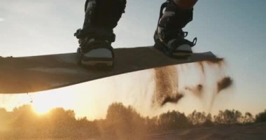 Genç ve güzel bir kadın kumsalda kumun üzerinde zıplıyor. Gün batımında snowboard 'a atlamaya çalışırken gülümseyen ve eğlenen bir kız. Spor konsepti, yaşam tarzı, kum kayağı, aşırı