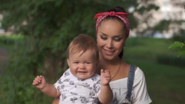 Elinde bebekle gülümseyen bir annenin aile portresi. Çocuk mutlu ve kameraya bakarak el sallıyor. Annesiyle bebeğinin sevimli bir sahnesi. Annelik kavramı, doğa..